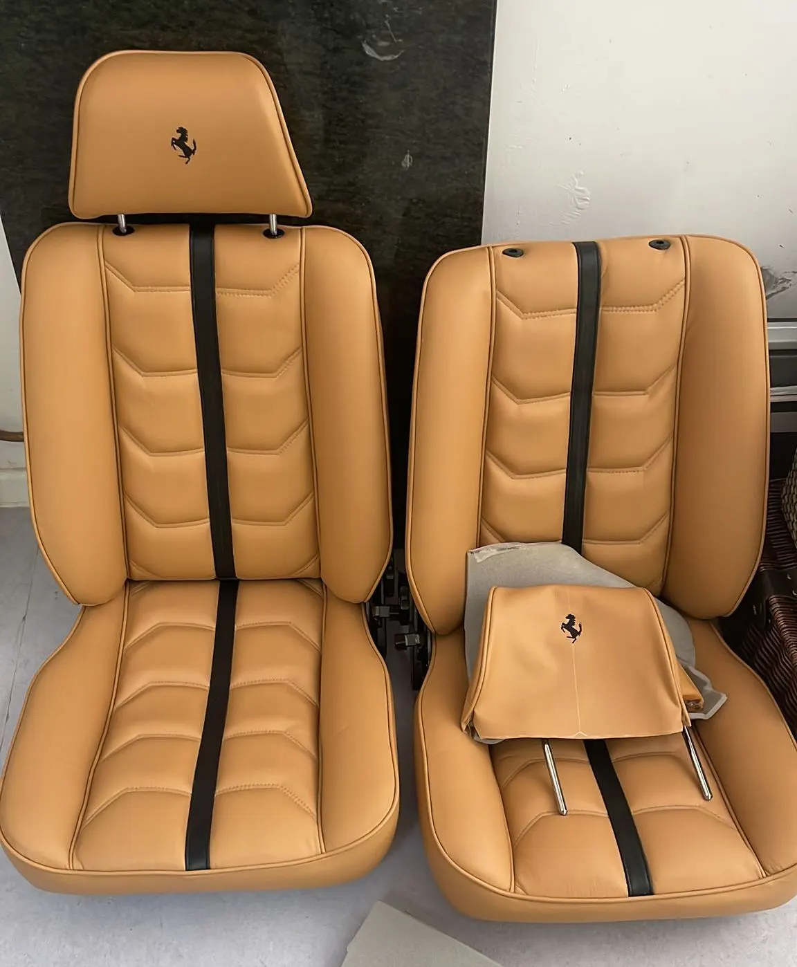 A pair of tan leather Ferrari seats with the prancing horse logo embroidered on each headrest